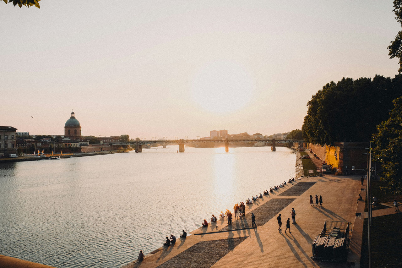 Bei Sonnenuntergang spazieren die Menschen entlang der Garonne in Toulouse und entspannen sich, während auf der anderen Seite des Flusses die Kuppel des La Grave-Krankenhauses zu sehen ist.