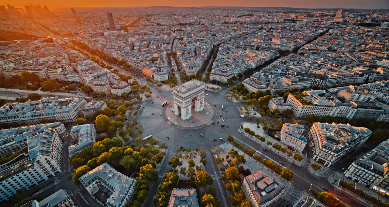 Luftaufnahme des Arc de Triomphe im Zentrum von Paris, mit sonnenbeschienenen Boulevards, die sich bei Sonnenuntergang strahlenförmig über die Stadt ausbreiten.