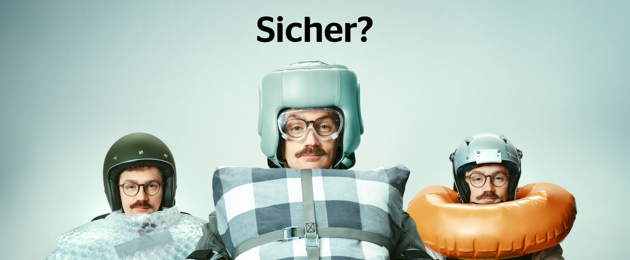 Mann mit verschiedenen umgebundenen Sicherheitsmaßnahmen (Kissen, Luftpolsterfolie, Schwimmring) hinter dem Autosteuer. Überschrift: Sicher?