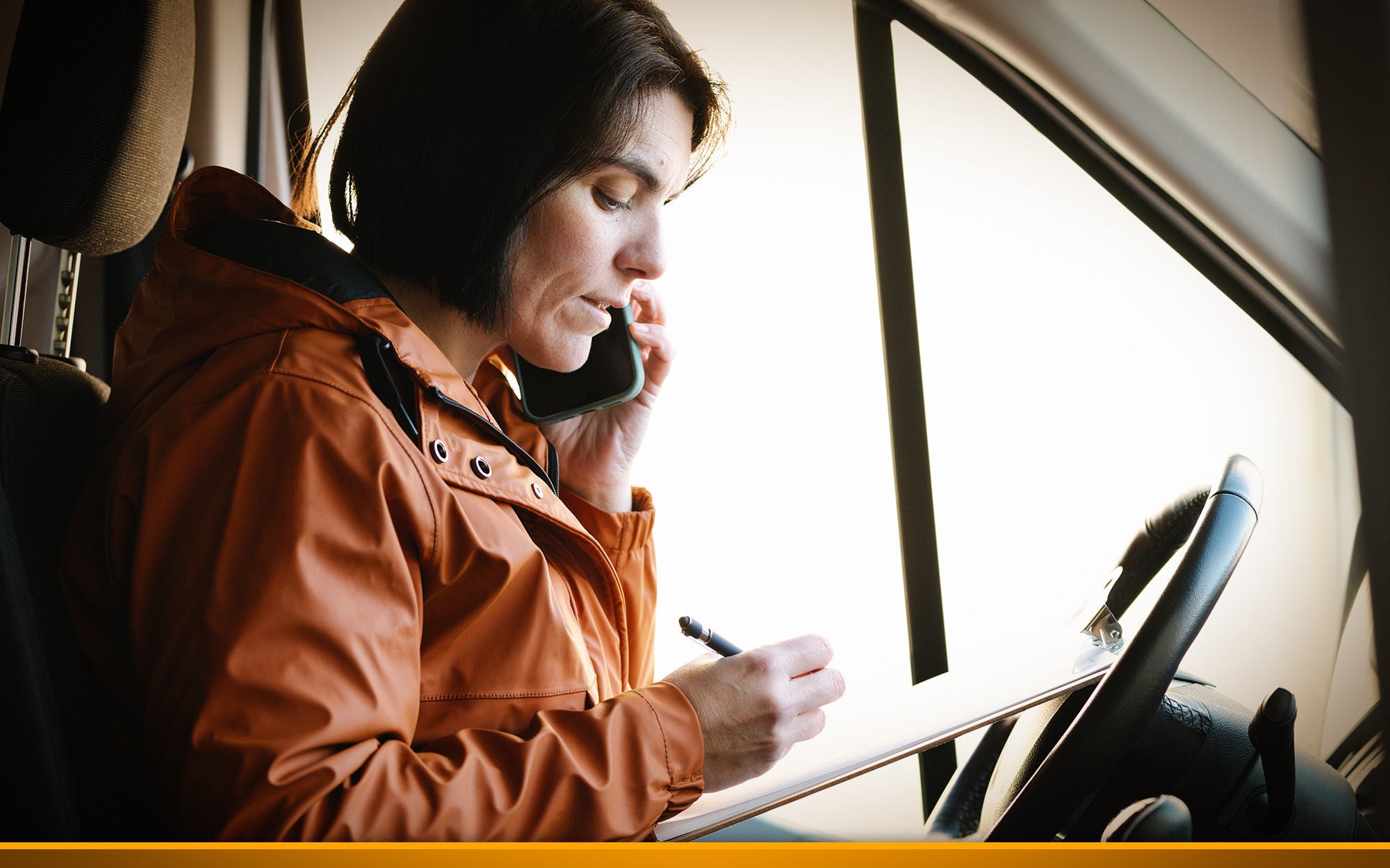 Woman talking on smartphone and writing notes on clipboard in truck