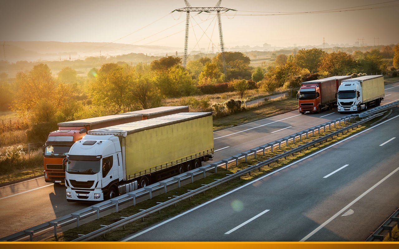 White and yellow semi trailer lorry truck overtaking red truck on a highway driving at beautiful dramatic sunset. Transportation vehicle