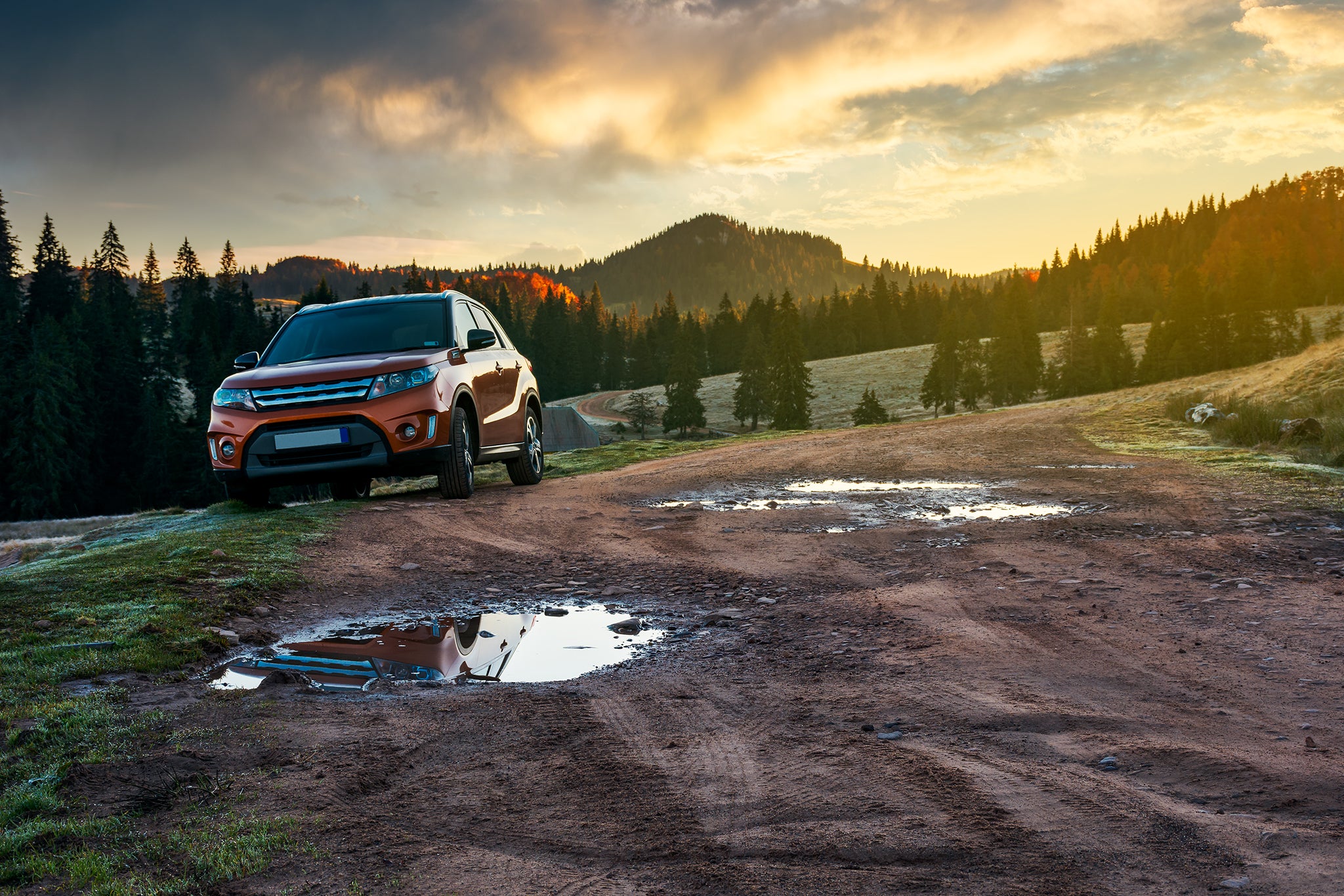 Orange suv parked on the country road near forest in mountains.