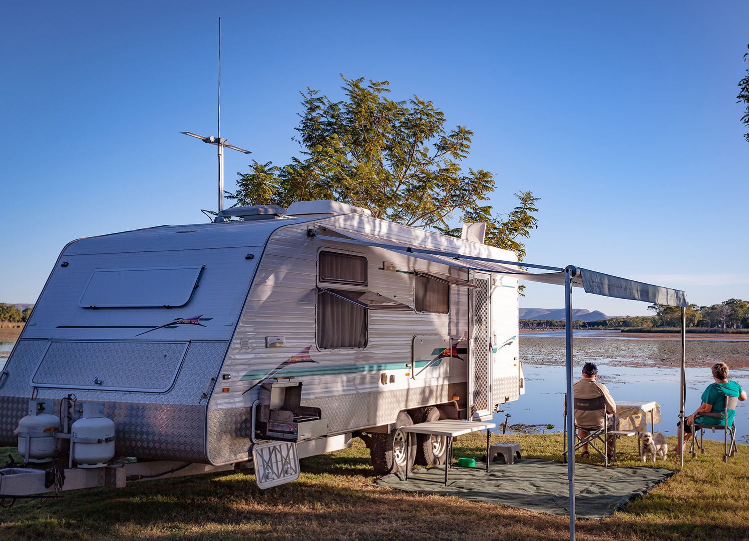Retired couple with small dog sitting enjoying view to lake next to a modern caravan, Retired couple with small dog sitting enjoying view to lake next A stunning location next to Lake Kununurra in the Kimberley of Western Australia