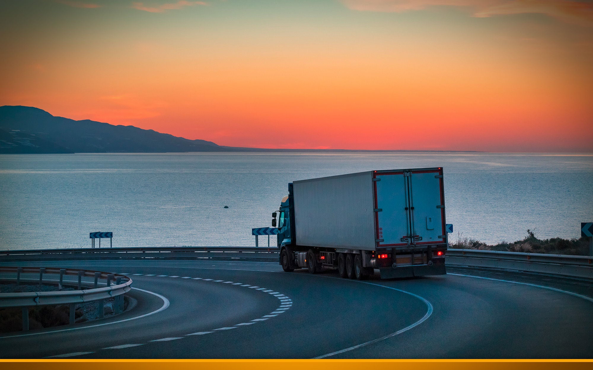 Truck on a mountain road with the sea and sunrise on the horizon.