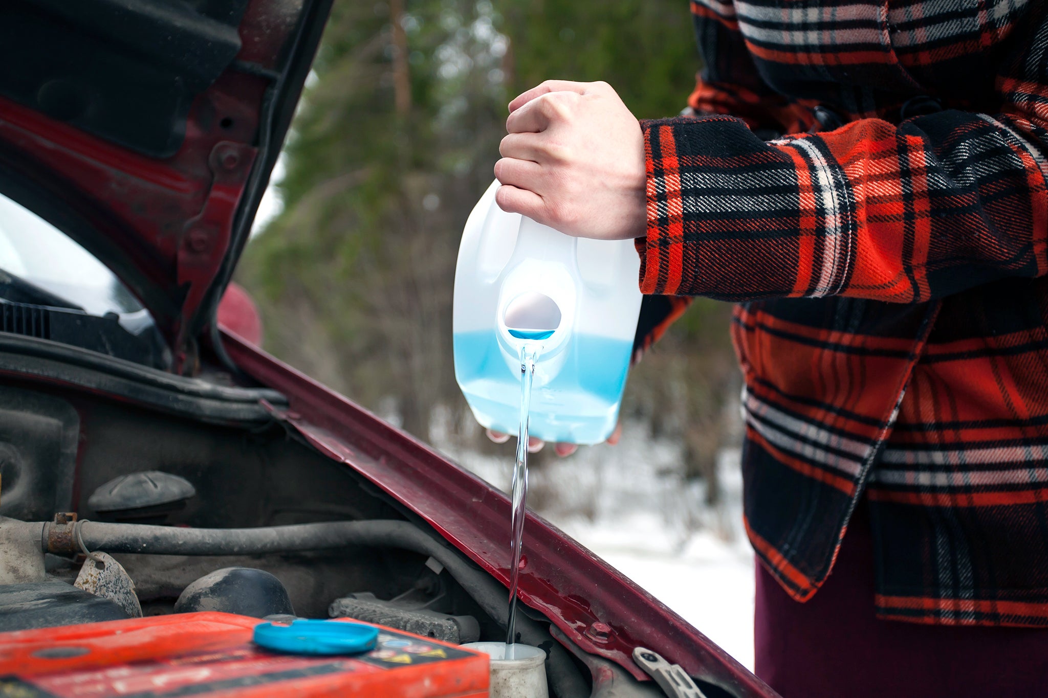 Filling in water Closeup shot of hands holding bottle with antifreeze washer fluid and pouring it into windshield washer tank in winter day.
