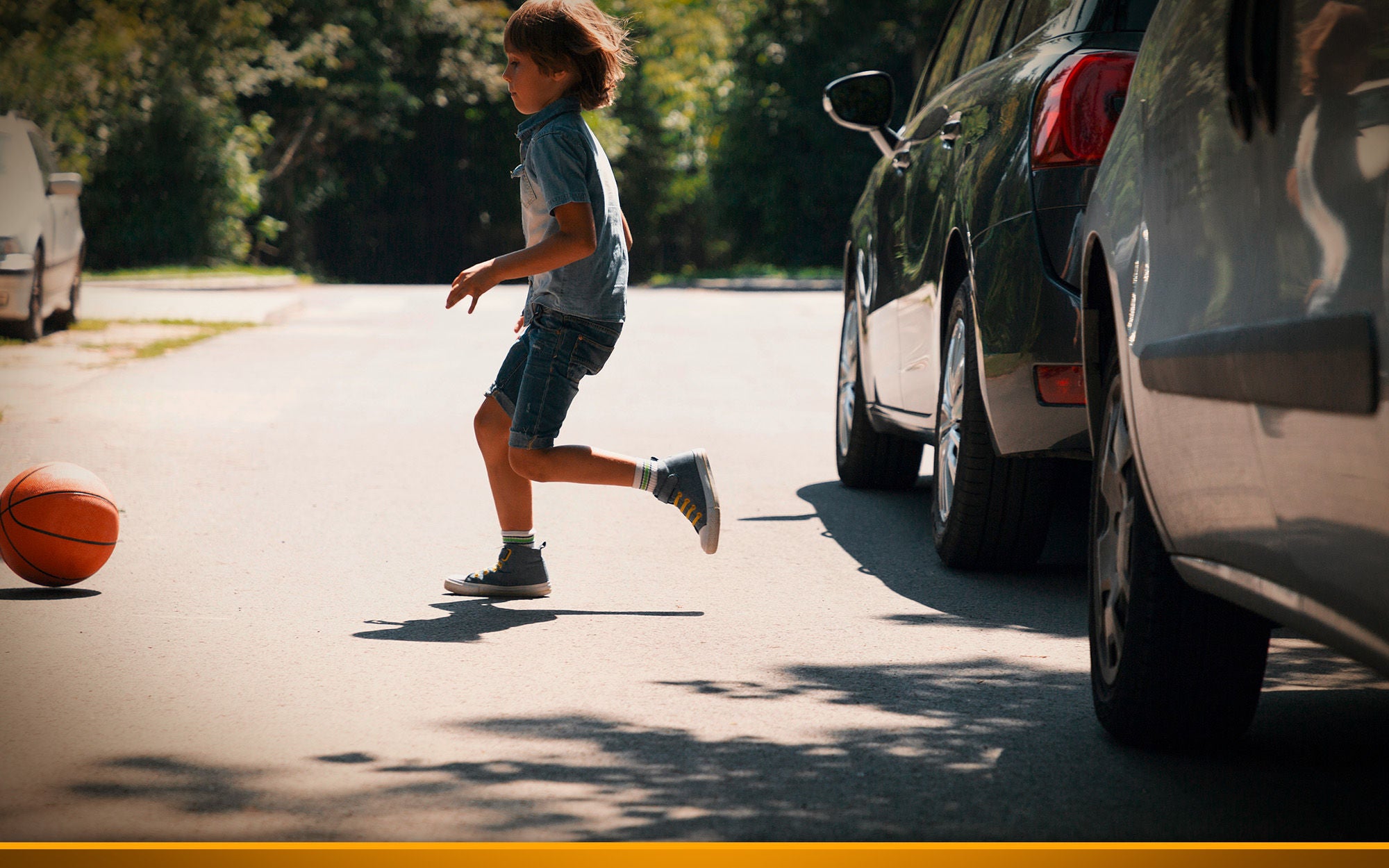 Careless boy running behind the ball on the road next to cars