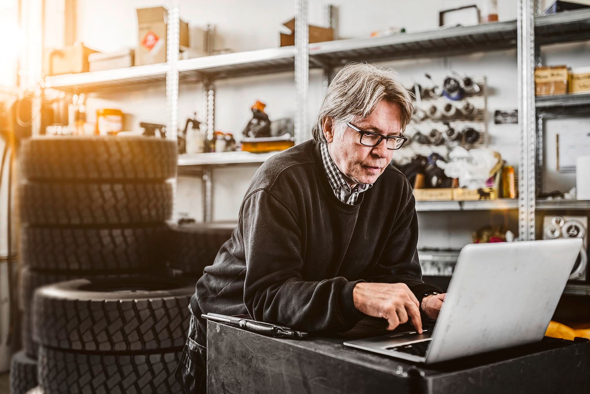 Male mechanic using laptop by shelves at tire shop