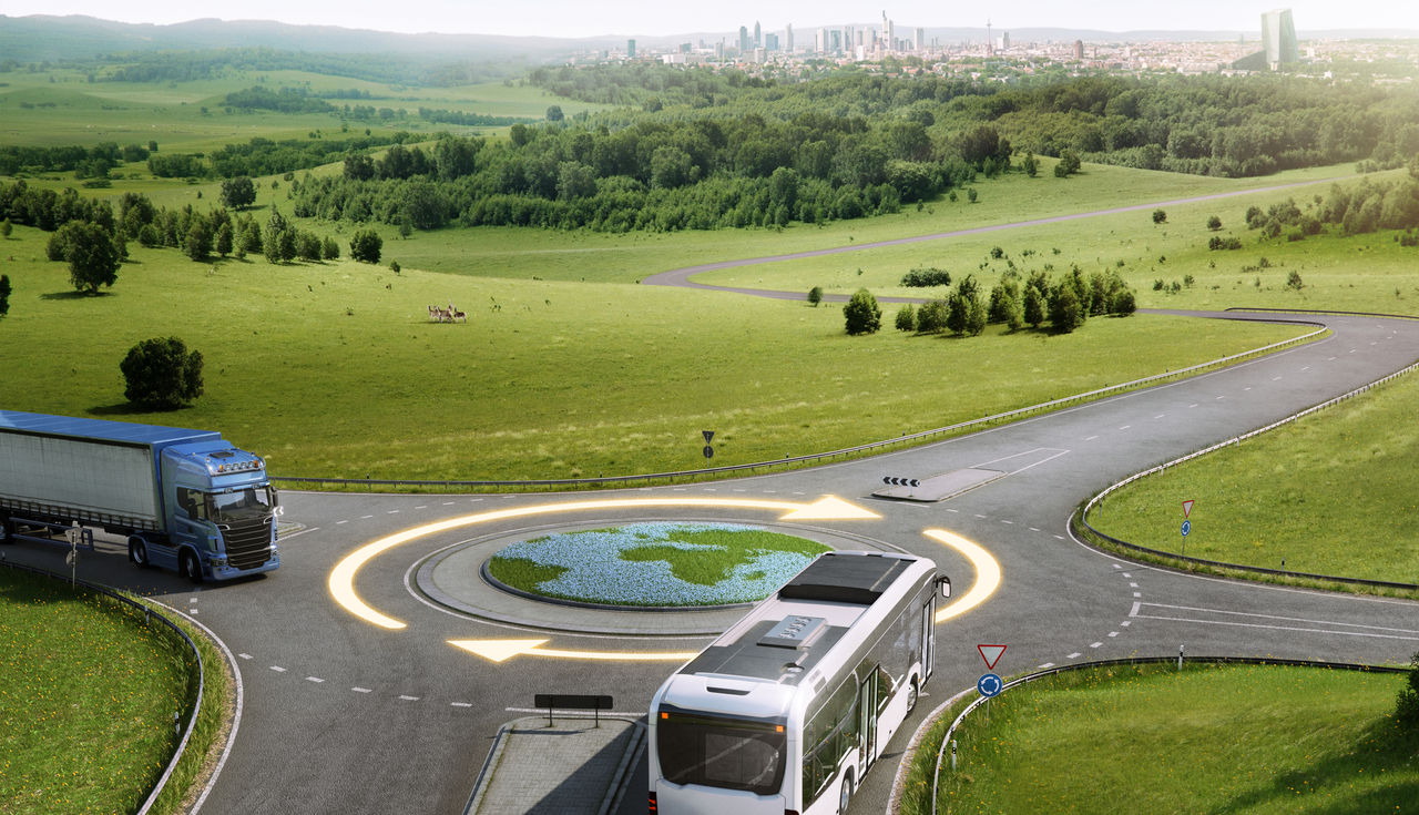 Two buses drive around a traffic circle, which looks like a globe, with lots of green space around and a two-part arrow going around the  traffice circle