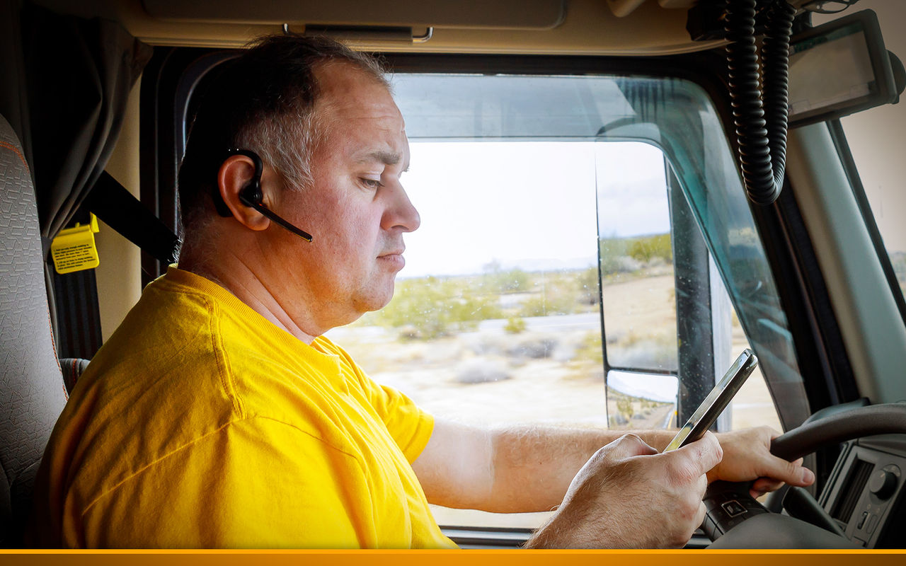 trucker in yellow t-shirt looking at his smartphone while driving