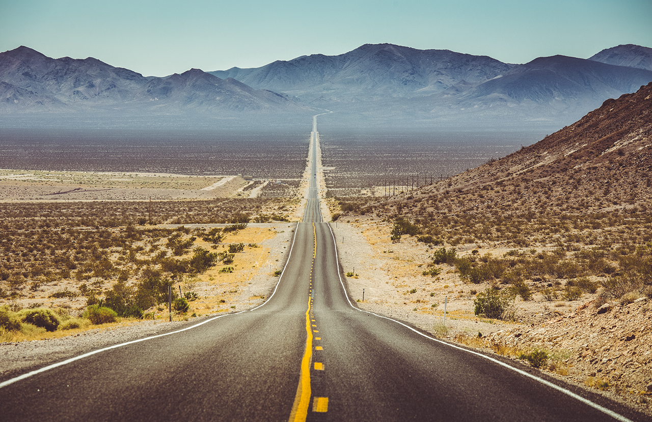 Classic vertical panorama view of an endless straight road running through the barren scenery of the American Southwest with extreme heat haze on a beautiful hot sunny day with blue sky in summer.