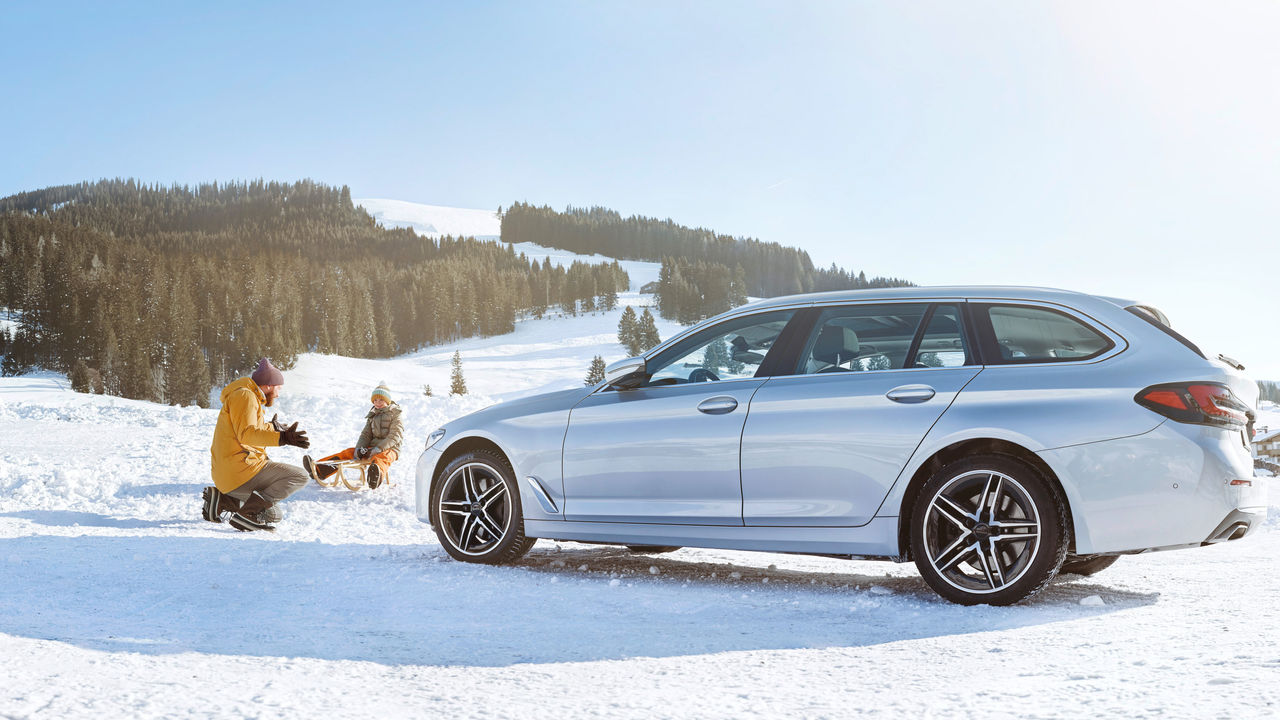 Farther and son with sledge in snow next to a car