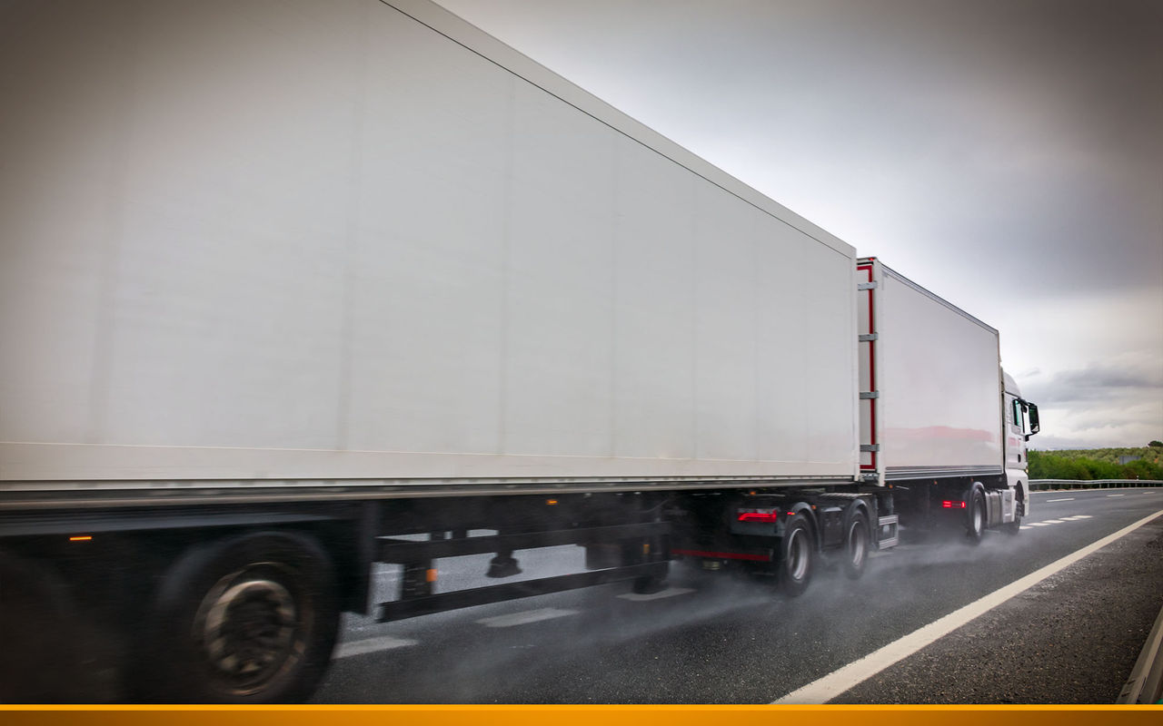Mega trailer or road train circulating on a day with bad weather due to rain, with the road wet and the wheels raising a cloud of water. 