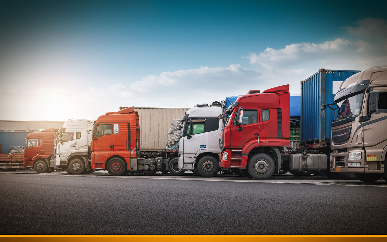 Row of parked trucks with trailers lined up along a road under a clear sky