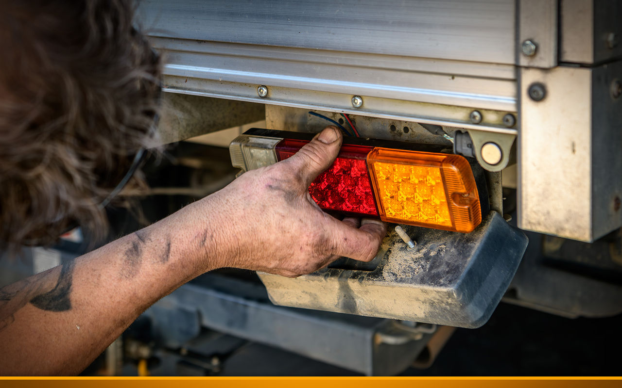 A mechanic repairs a tail light on a ute truck.