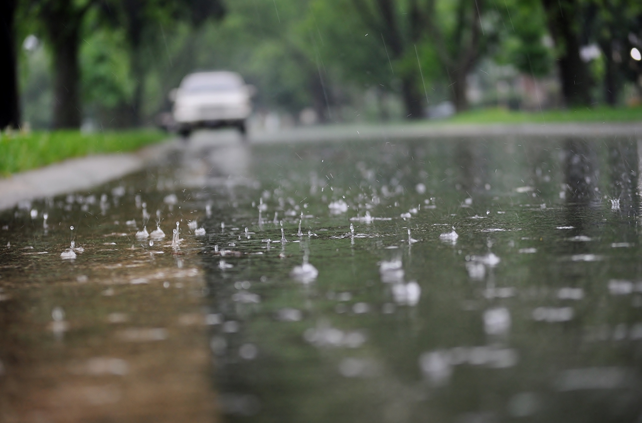 All Season tires Wasser fließt bei starkem Regen entlang der Straßenkante. Nahaufnahme von spritzenden Regentropfen und Luftblasen.