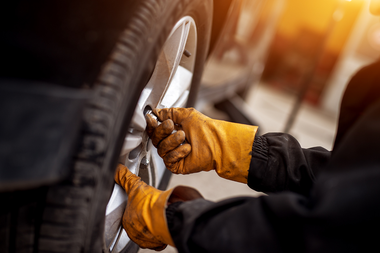 Ein erfahrener Mechaniker mit orangefarbenen Handschuhen schraubt ein Rad an einem Auto fest.